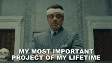 a man with a bandage on his head is smoking a cigarette and says " my most important project of my lifetime "