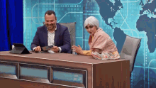a man and a woman are sitting at a desk with a map of the world in the background