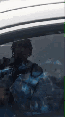 a man in a blue jacket is reflected in the windshield of a silver car