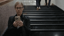 a woman is sitting on a set of stairs looking at her cell phone