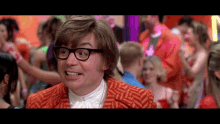 a man wearing glasses and an orange suit is smiling in front of a crowd