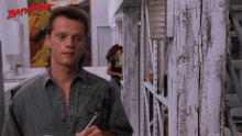 a man in a grey shirt is holding a wrench in front of a baywatch poster
