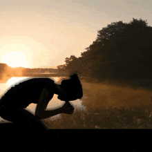 a silhouette of a woman kneeling in front of a body of water