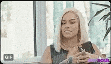 a woman with blonde hair is sitting in front of a window with her hands on her chest .