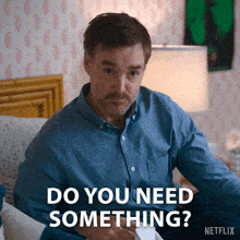a man in a blue shirt is sitting on a bed and says do you need something netflix