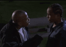 two men are standing next to each other and looking at each other in a dark room .