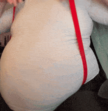 a woman wearing a white shirt and red suspenders has a very large belly