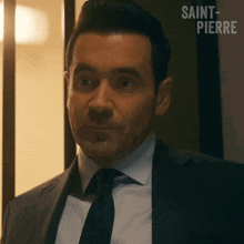 a man in a suit and tie is standing in front of a wall that says saint-pierre