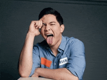 a man in a blue shirt is sticking his tongue out while sitting at a table .