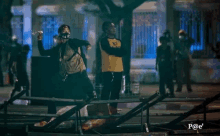 a man wearing a mask throws a bottle over a fence while another man watches