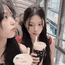 a girl drinking from a cup with a straw while another girl looks on