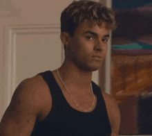 a young man wearing a black tank top and a chain around his neck looks at the camera