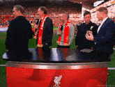 a group of men are standing around a table with the liverpool logo on it