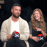 a man and a woman are sitting next to each other and the man is holding a red button with an x on it