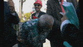 a man wearing a red hard hat and sunglasses is talking to another man in a suit
