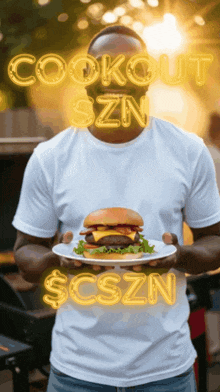 a man in a white shirt holds a plate with a hamburger on it in front of a sign that says cookout szn