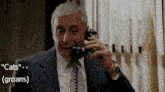 a man in a suit and tie is talking on a phone with the words " cats " and " groans " above him