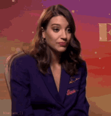 a woman in a purple suit is sitting in a chair and making a funny face