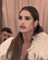a woman wearing a fur coat and earrings looks at the camera .