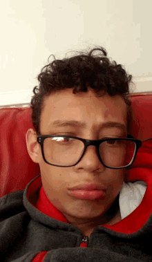 a boy with curly hair wearing glasses and a red sweatshirt