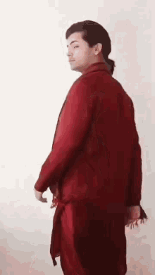a man in a red suit is standing in front of a white wall and looking at the camera .