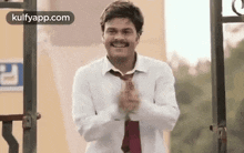 a man in a white shirt and red tie is clapping his hands in front of a building .