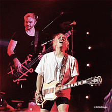 a man playing a bass and a woman playing a guitar on a stage with a red background