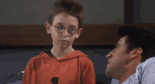 a boy wearing glasses and an orange shirt with the number 1 on it talks to a man in a hospital gown