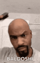 a bald man with a beard is holding a brush in his hand .