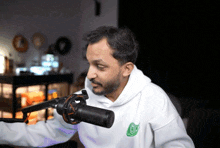 a man wearing a white hoodie with a green leaf on the front is talking into a microphone