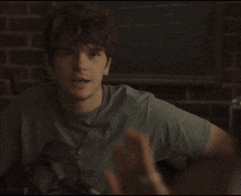 a young man in a grey shirt is sitting in front of a chalkboard