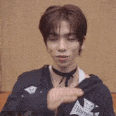 a young man wearing a black hoodie and a choker is waving his hand .