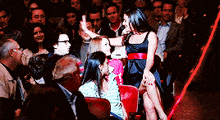 a woman in a black dress is sitting on a stage in front of a crowd