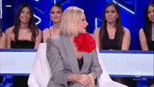 a woman with a red flower in her mouth is sitting in front of a group of women with the letters mediaset on the bottom