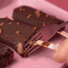 a person is holding a fork over a piece of chocolate