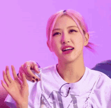 a woman with pink hair is wearing a white t-shirt and glasses .
