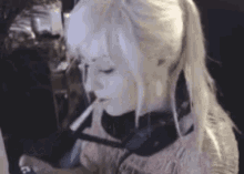 a woman with white hair is smoking a cigarette in front of a computer .
