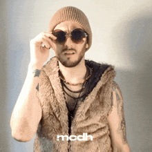 a man wearing sunglasses and a fur vest has the word mcdh on the bottom right