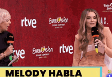 two women standing in front of a red background that says eurovision song contest