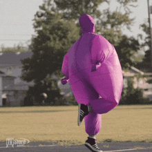a person in a purple inflatable suit is running in a field with the tv store button in the corner