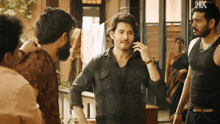 a man in a black shirt is talking on a cell phone while standing next to another man .