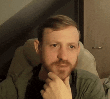a man with a beard is sitting in a chair with his hand to his chin