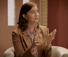a woman sitting in a chair with her hands outstretched and a brooch that has the letter c on it