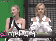 two women are sitting at a table with their hands folded in front of them .
