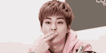 a young man in a pink hoodie is making a funny face while holding his finger to his mouth .