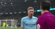 a man in a manchester city jersey is talking to another man on a soccer field