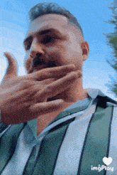 a man wearing a green and white striped shirt has his hand on his face
