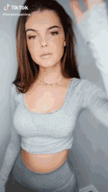 a woman in a grey crop top is taking a selfie with tiktok written on the bottom