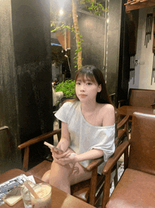 a woman sits at a table with her legs crossed holding a cell phone