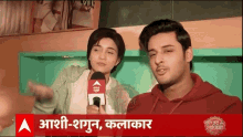 a man and a woman are sitting in front of a sign that says ' aashi-shagun kalakar '